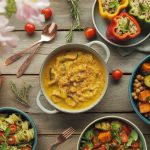 Colorful array of vegetarian dinner recipes including pasta, curry, and buddha bowls arranged on rustic wooden table with fresh vegetables