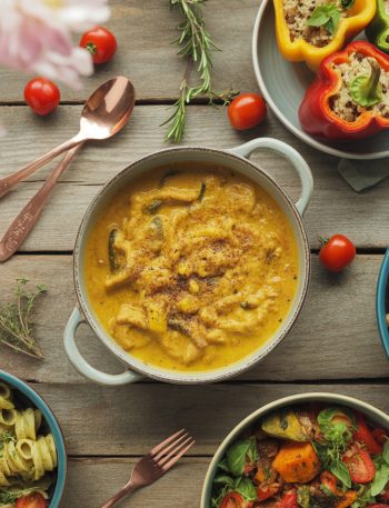 Colorful array of vegetarian dinner recipes including pasta, curry, and buddha bowls arranged on rustic wooden table with fresh vegetables