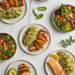 Assortment of colorful low calorie dinner recipes including grilled chicken, zucchini noodles, and fresh vegetables arranged on a marble countertop