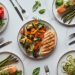 Variety of healthy dinner recipes including grilled chicken, salmon, and vegetables arranged on marble surface