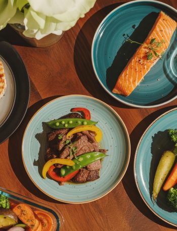 Variety of high protein dinner recipes including grilled chicken, salmon, and beef arranged on a rustic wooden table with weights in background