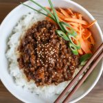 Overhead view of Korean ground beef rice bowl with glazed meat, white rice, sesame seeds and green onion garnish in white bowl