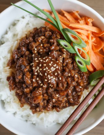 Overhead view of Korean ground beef rice bowl with glazed meat, white rice, sesame seeds and green onion garnish in white bowl