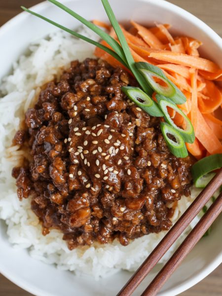 Overhead view of Korean ground beef rice bowl with glazed meat, white rice, sesame seeds and green onion garnish in white bowl