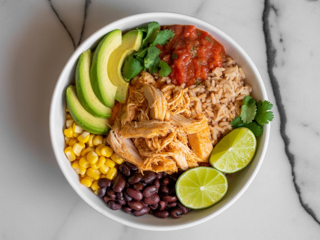 Mexican shredded chicken bowl with rice, black beans, avocado, and fresh toppings