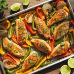 Colorful sheet pan chicken fajitas with seared chicken strips, roasted bell peppers and onions garnished with cilantro and lime wedges