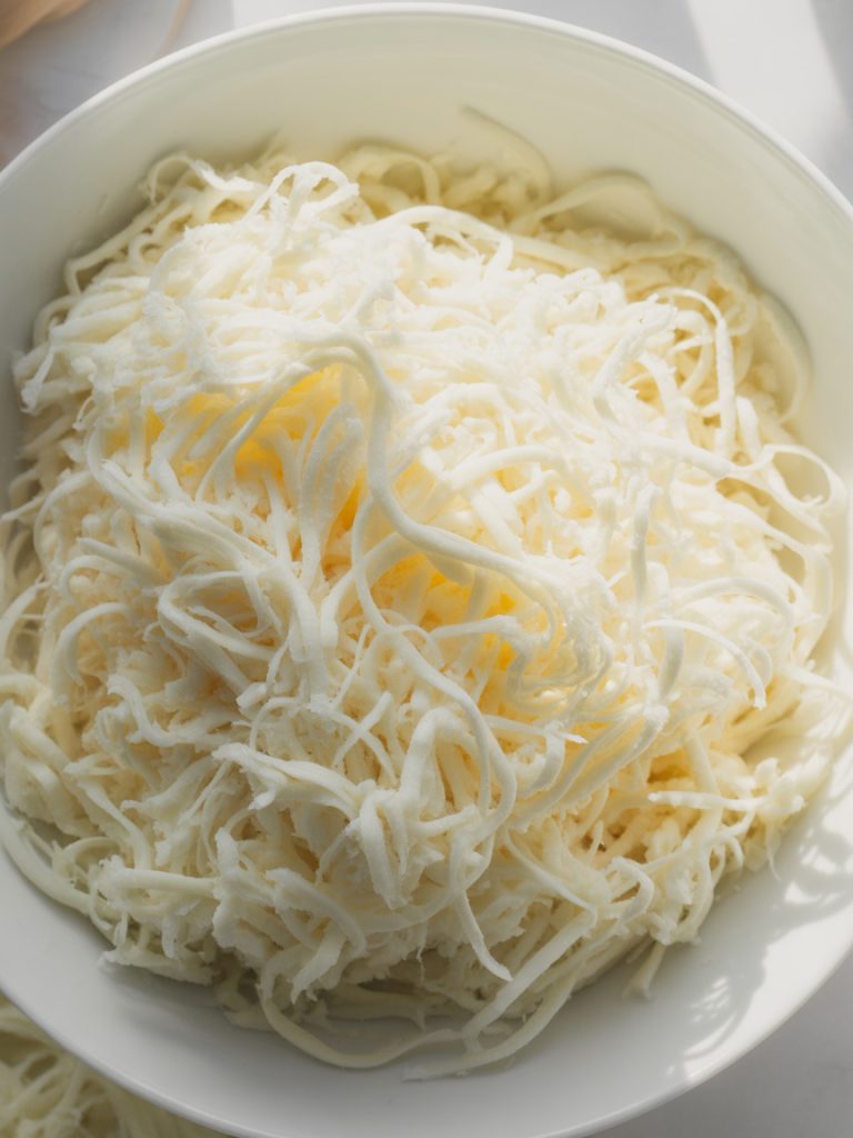 White bowl filled with shredded mozzarella cheese showing stringy texture for pizza topping