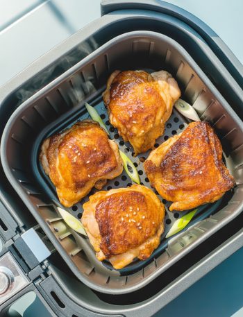 Crispy golden-brown teriyaki chicken thighs in air fryer basket with caramelized glaze and sesame seed garnish