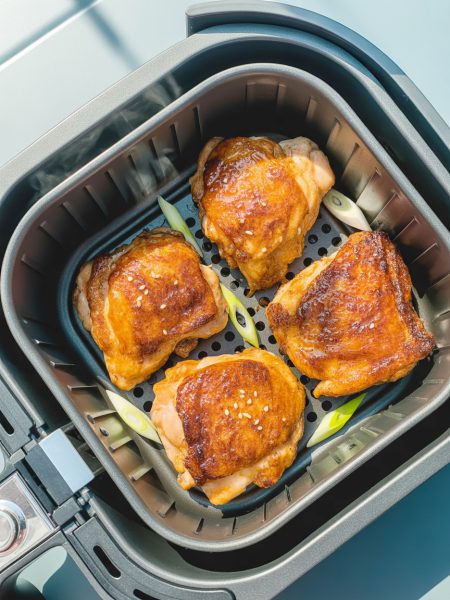 Crispy golden-brown teriyaki chicken thighs in air fryer basket with caramelized glaze and sesame seed garnish