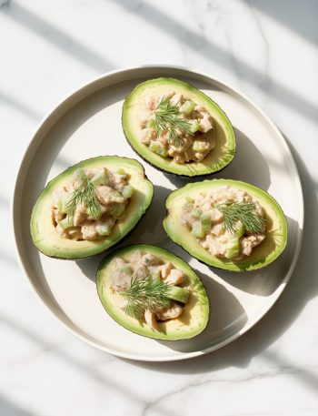 Four avocado halves stuffed with creamy chicken salad garnished with fresh dill on a white plate