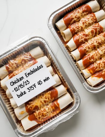 Two aluminum foil pans of assembled chicken enchiladas wrapped and labeled ready for freezer storage