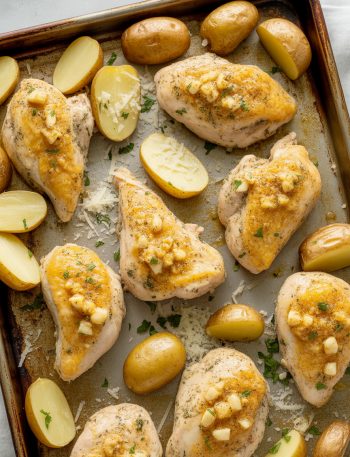 Sheet pan of golden roasted chicken and crispy potatoes coated in garlic parmesan butter, garnished with parsley