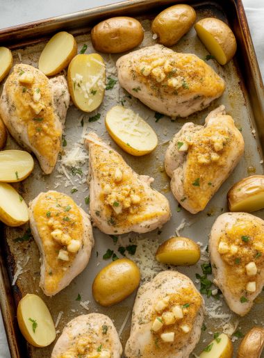 Sheet pan of golden roasted chicken and crispy potatoes coated in garlic parmesan butter, garnished with parsley