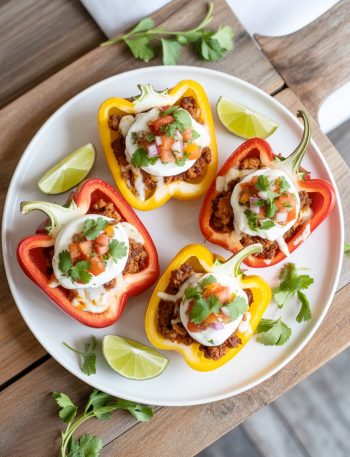 Colorful bell pepper halves stuffed with seasoned ground turkey, black beans, and topped with Greek yogurt, salsa, and fresh cilantro on a white plate