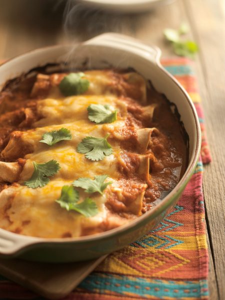 Homemade chicken enchiladas with red sauce and melted cheese in rustic baking dish garnished with cilantro