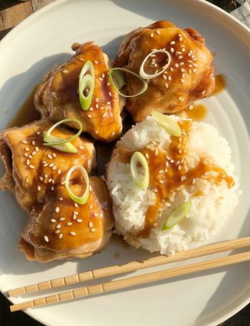 Golden-brown honey teriyaki chicken thighs with glossy amber glaze, garnished with sesame seeds and green onions, served with rice