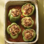 Overhead view of traditional green stuffed peppers with ground beef and tomato sauce in baking dish
