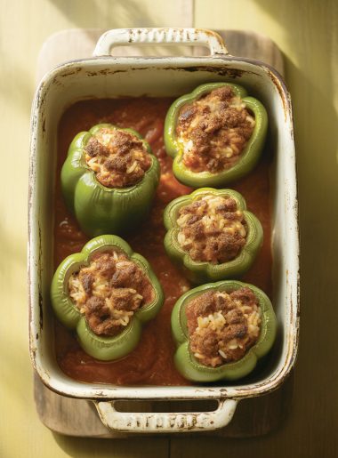 Overhead view of traditional green stuffed peppers with ground beef and tomato sauce in baking dish