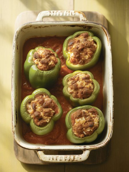 Overhead view of traditional green stuffed peppers with ground beef and tomato sauce in baking dish
