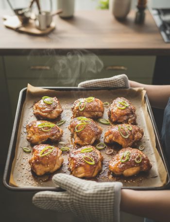 Golden-brown teriyaki chicken thighs on baking sheet with caramelized glaze, fresh from oven, garnished with sesame seeds