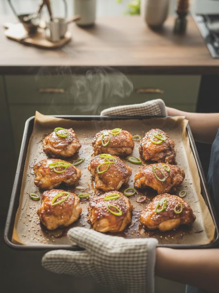 Golden-brown teriyaki chicken thighs on baking sheet with caramelized glaze, fresh from oven, garnished with sesame seeds