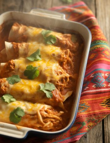 Shredded chicken enchiladas with red sauce and melted cheese in a baking dish garnished with cilantro