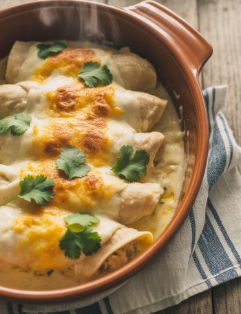 Creamy sour cream chicken enchiladas in a baking dish topped with melted cheese and fresh cilantro