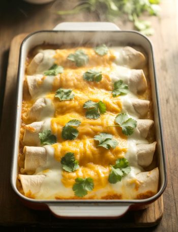 Baking dish of white chicken enchiladas covered in creamy sauce and golden melted cheese, garnished with cilantro