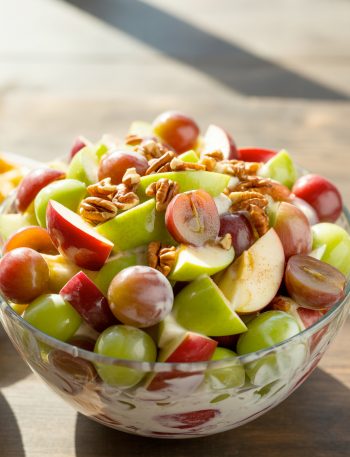 Glass bowl of creamy cinnamon apple grape salad with pecans on top