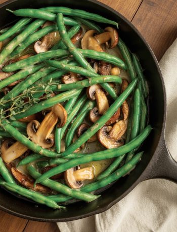 Sautéed green beans with golden mushrooms in butter sauce in cast iron skillet