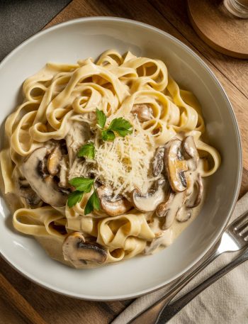 Creamy mushroom pasta with fettuccine in a white bowl topped with parmesan cheese and fresh parsley