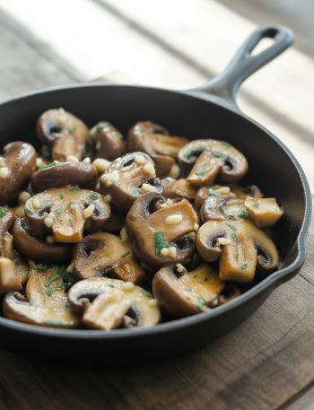 Cast iron skillet filled with golden sautéed mushrooms in garlic butter with fresh herbs