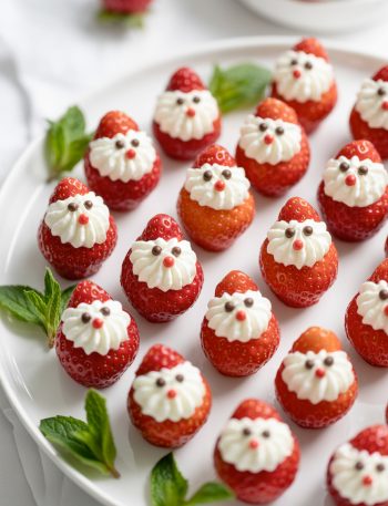 Adorable strawberry Santas with cream cheese beards and whipped cream hats arranged on white platter