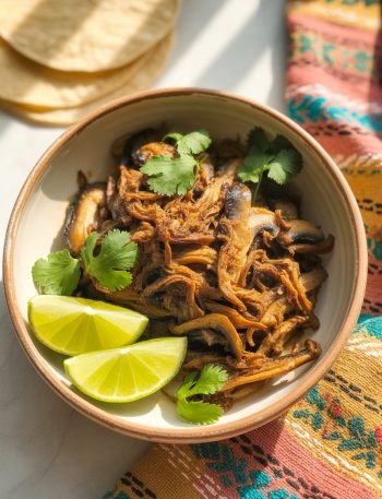 Crispy vegan carnitas made with mushrooms in a ceramic bowl garnished with cilantro and lime
