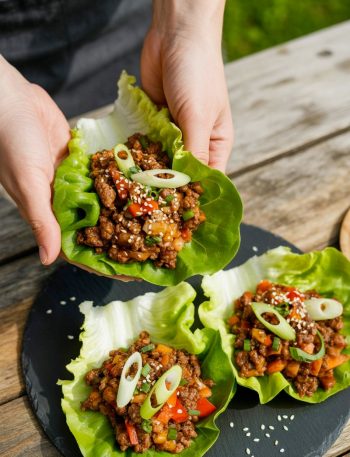 Asian beef lettuce wraps on black plate with sesame seeds and green onions