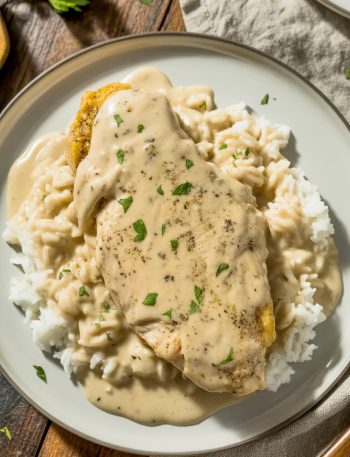 Creamy smothered chicken in rich gravy served over fluffy white rice with fresh parsley garnish