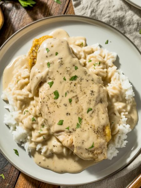 Creamy smothered chicken in rich gravy served over fluffy white rice with fresh parsley garnish