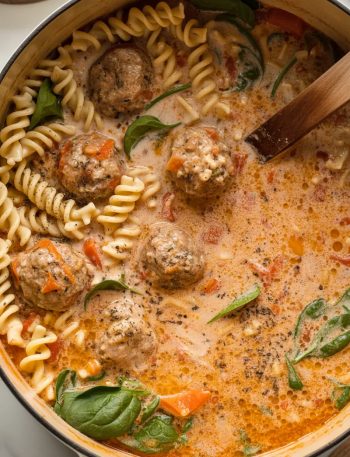Large pot filled with creamy Italian meatball soup showing meatballs, rotini pasta, and fresh spinach in rich orange-red tomato-cream broth