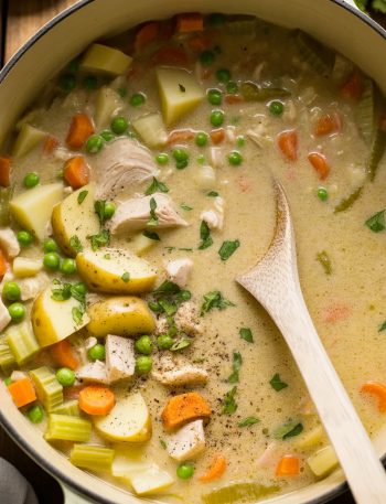 Large pot filled with creamy leftover turkey soup showing chunks of turkey, yellow potatoes, orange carrots, celery, and fresh parsley in rich cream broth with white wooden spoon