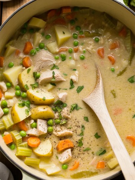 Large pot filled with creamy leftover turkey soup showing chunks of turkey, yellow potatoes, orange carrots, celery, and fresh parsley in rich cream broth with white wooden spoon