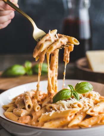 Creamy tomato garlic pasta with cheese pull on gold fork showing rich sauce