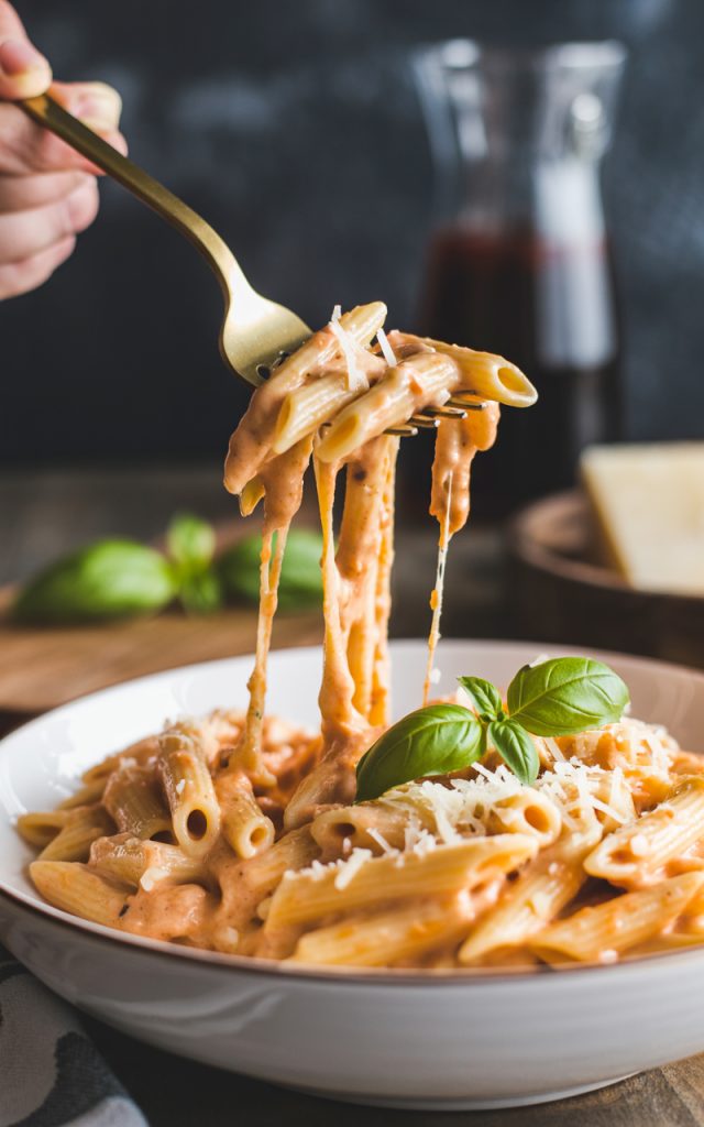 Creamy tomato garlic pasta with cheese pull on gold fork showing rich sauce