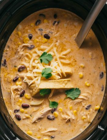 Creamy chicken tortilla soup in slow cooker with shredded chicken, beans, corn, and toppings