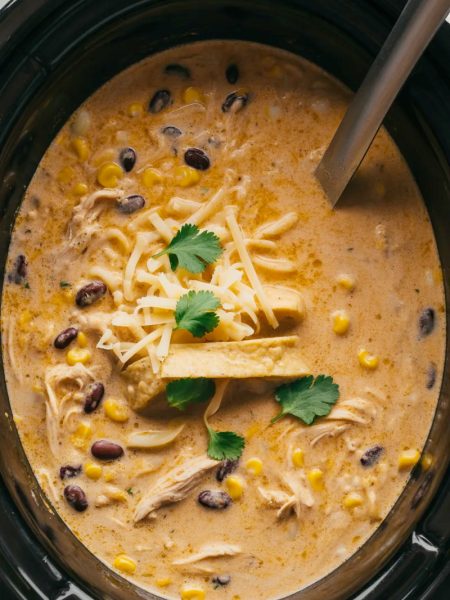 Creamy chicken tortilla soup in slow cooker with shredded chicken, beans, corn, and toppings