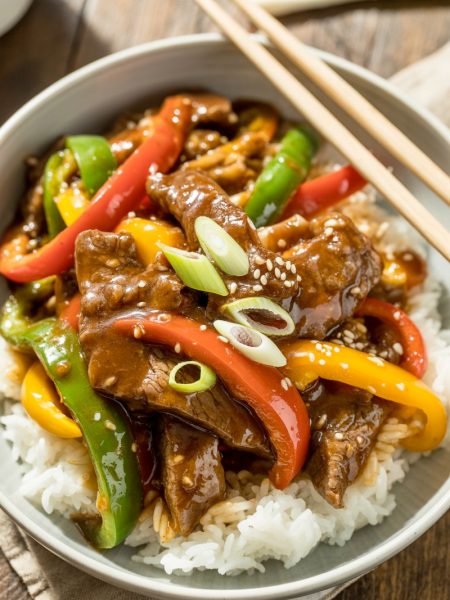 Pepper steak with colorful bell peppers in white bowl over rice
