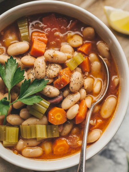White ceramic bowl filled with traditional Greek fasolatha white bean soup showing creamy white beans, orange carrots, celery, and fresh parsley in tomato-based broth