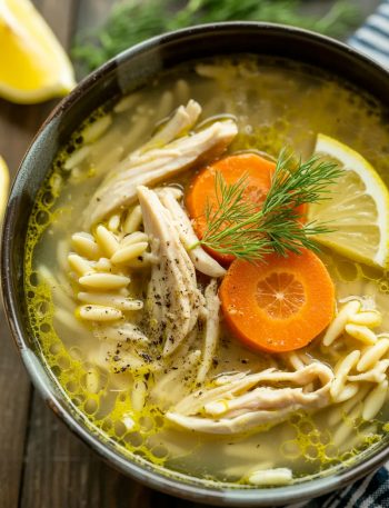 Greek lemon chicken soup with orzo pasta, shredded chicken, carrots, and fresh dill in a black bowl