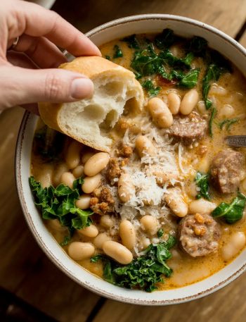 Bowl of creamy Italian sausage and white bean soup with kale, topped with Parmesan cheese and crusty bread for dipping