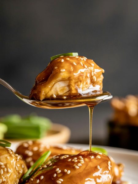 Honey butter chicken bite on spoon with glossy caramelized glaze dripping