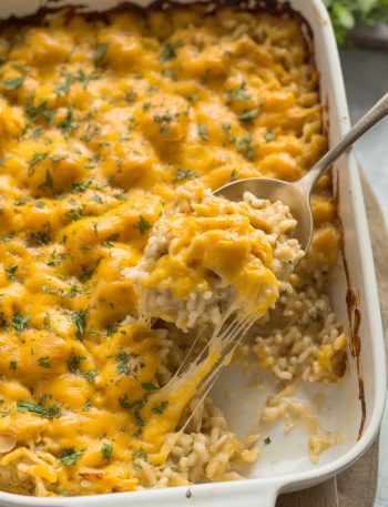 Golden bubbly chicken rice casserole with melted cheddar cheese, fresh parsley garnish, and cheese pull from serving spoon